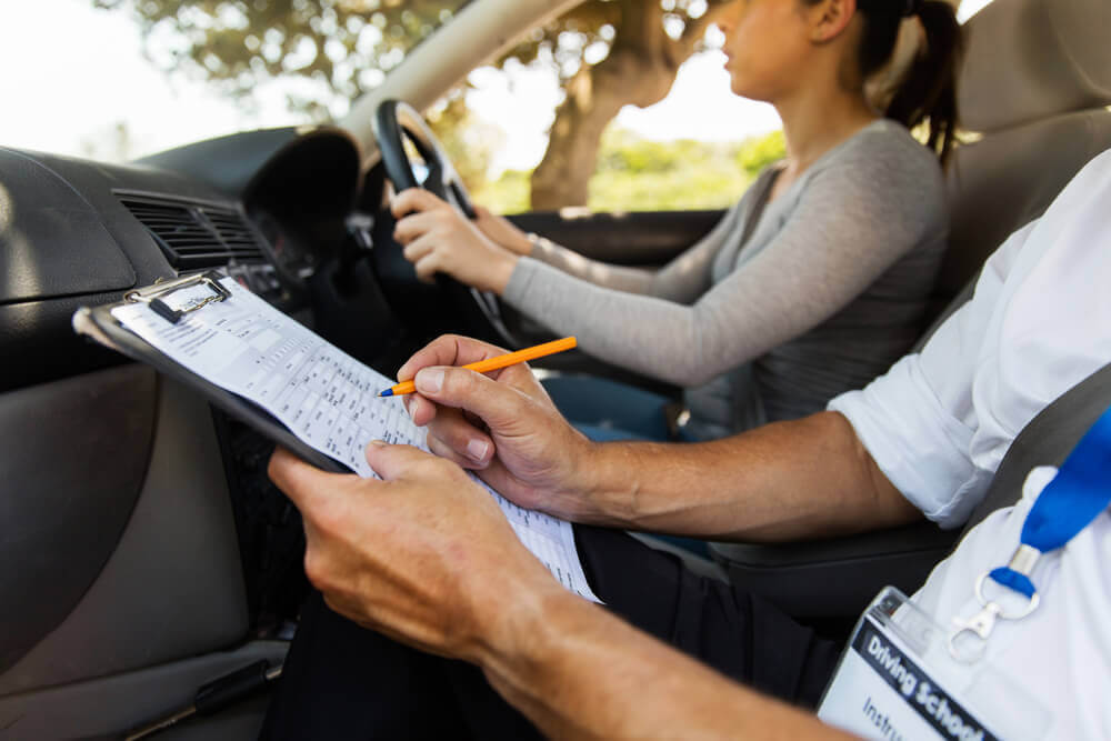 A driving school Mandurah instructor marking a student in the car with a clipboard