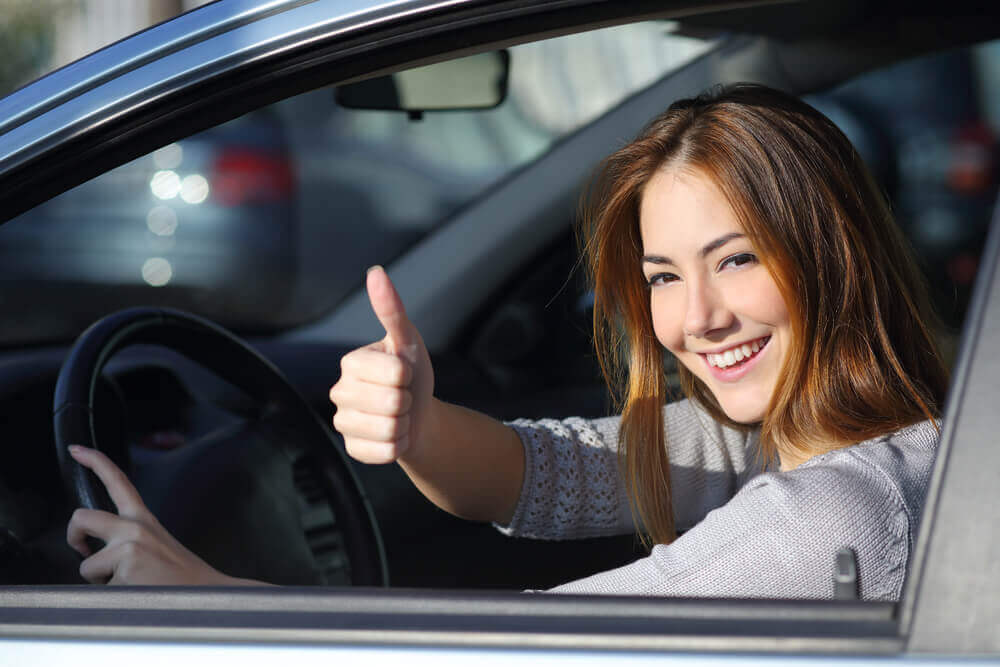 young female learner driver giving the thumbs up out of a window after a successful driving test